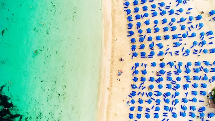 Poster Aerial bird's eye view of Makronissos organised beach coastline, Ayia Napa, Famagusta, Cyprus from above. Blue aligned umbrellas, golden sand, parasols, people sunbathing sun beds clean turquoise sea. © f8grapher