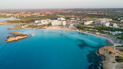 Aerial bird's eye view of famous Nissi beach coastline, Ayia Napa, Famagusta, Cyprus.Landmark tourist attraction islet bay at sunrise with golden sand, sunbeds, sea restaurants in Agia Napa from above