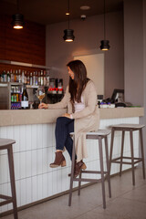 joyful young woman sitting at the bar counter with a glass of wine and a bottle of wine