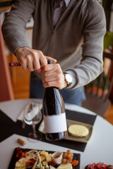 man opens a bottle of wine with a corkscrew over a table with many food and snacks