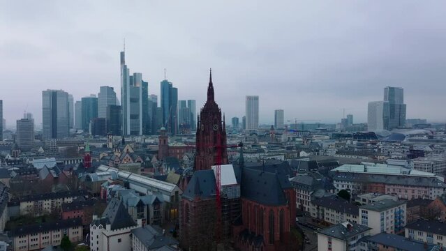 Forwards fly above buildings in urban borough around tower of Frankfurter Dom. Modern office towers in business centre in background. Frankfurt am Main, Germany