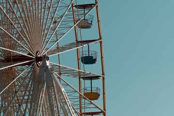 Detail of a Ferris wheel with different-colored gondolas against a blue sky background.