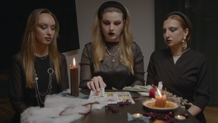 4K. Three female witches in a dark room reading tarot cards