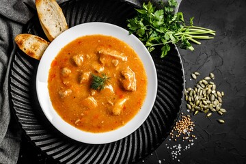 Top view of tasty tomato soup with meat, toasts, greens, and spices on black table