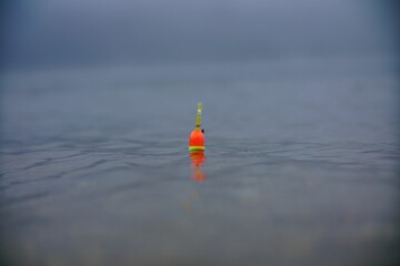 Orange and green fishing bobber floating in the water © Ufuk Bayram/Wirestock Creators