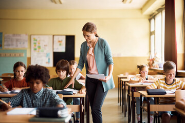 Smiling teacher assisting elementary student during class in classroom.