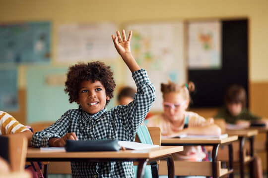 Happy African American kid raising his arm to ask question during class at elementary school.