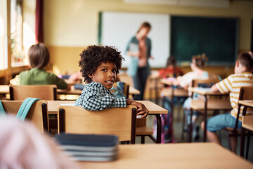 Happy black schoolboy having class in classroom and looking at camera.