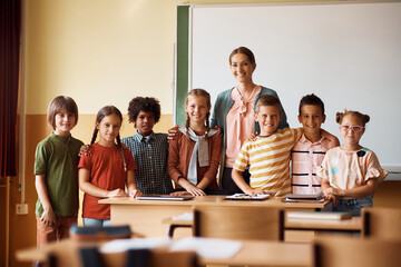 Portrait of happy school kids with their teacher in classroom looking at camera.