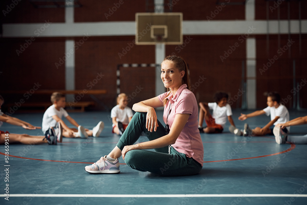 Wall mural happy physical education teacher with group of students in background at school gym.