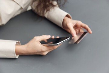 Cool Mockup offer. Side of view on hands of tanned Latin woman in linen shirt with credit debit card and modern smartphone on dark gray background. Copy space. Shopaholic lady doing online shopping.