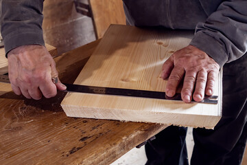 male carpenter marks out a wooden board with a ruler and pencil in his home workshop. working with wood.