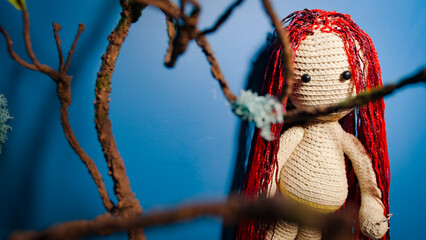 Knitted doll with dreadlocks hanging on wall. Handmade soft toy with hairstyle on blue wall. Concept of interior and beauty.