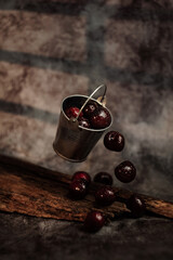 Ripe cherries with dew drops in an iron bucket on a dark background.