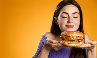 Smiling woman smells her tasty fresh burger from restaurant delivery. Girl holds cheeseburger on...