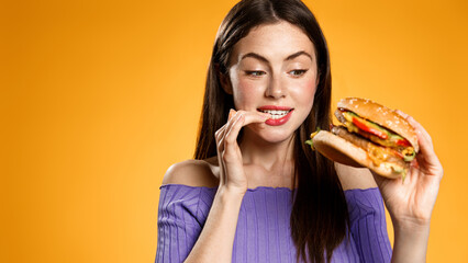 Hungry girl looks at tasty burger, wants to eat it. Woman bites her finger while holding cheeseburger fast food. Concept of eating out and restaurant delivery