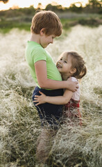 Naklejka na ściany i meble Children brother and sister hug standing in a field with tall grass outside, boy and girl walk outside in nature
