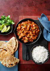 Chicken tikka masala spicy curry meat food Butter chicken, rice and naan bread on red vine dark background. Traditional Indian dish, top view, close up, copy space.