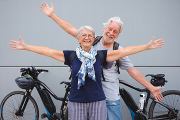 Cheerful senior couple with outstretched arms enjoying sport activity with their electric bicycles...