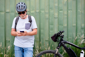 Attractive senior man with helmet and backpack using mobile phone while enjoying sport activity...