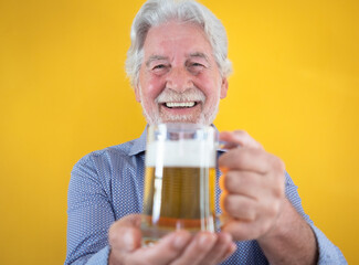 Handsome happy senior man holding a glass of fresh blonde beer - caucasian bearded elderly man on yellow background