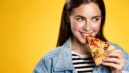 Image of girl smiling while biting slice of pizza, happy face at pizzeria restaurant, yellow...