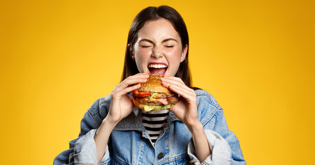 Girl bites cheeseburger with pleasure. Woman eating hambuger, order burger for takeaway food delivery at fastfood restaurant - obrazy, fototapety, plakaty