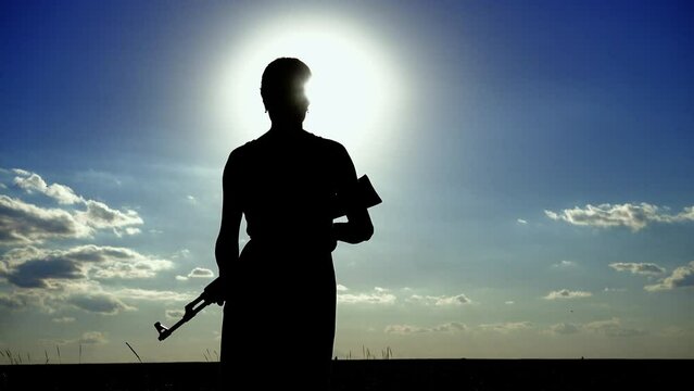 Ukraine War. A young woman with a Kalashnikov assault rifle is training in the field. Silhouette of a girl with a Kalashnikov assault rifle. The concept of war, terrorism, aggression against Ukraine.