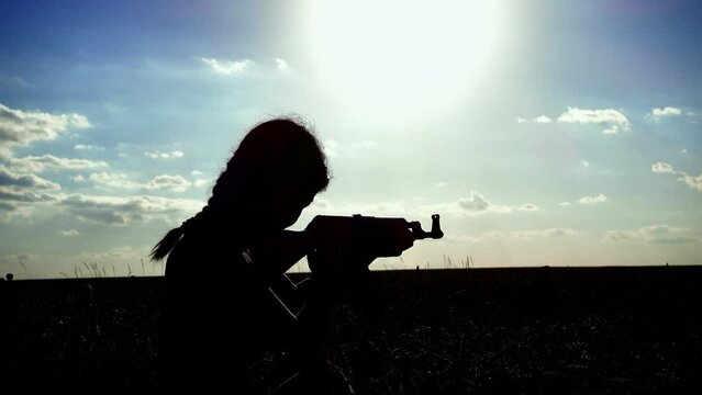 Ukraine War. Portrait of a young woman with a Kalashnikov assault rifle is training in the field. Close-up silhouette of a girl with a Kalashnikov assault rifle. The concept of war, terrorism, aggress