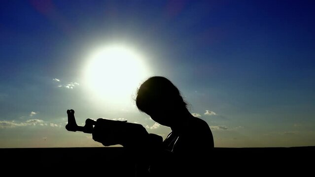 Ukraine War. Portrait of a young woman with a Kalashnikov assault rifle is training in the field. Close-up silhouette of a girl with a Kalashnikov assault rifle. The concept of war, terrorism, aggress