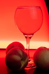 Drink, glass of sparkling wine with peaches around and colored light in the background, light painting style photo, selective focus.