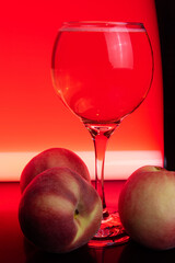 Drink, glass of sparkling wine with peaches around and colored light in the background, light painting style photo, selective focus.