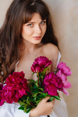 a beautiful young brunette woman in a white shirt with a bouquet of peonies.