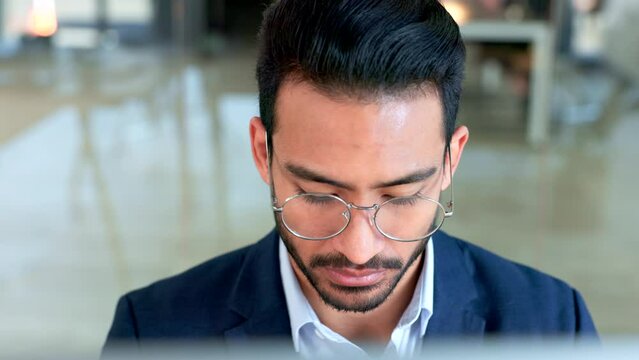 Focused male copywriter writing a script using a computer inside an office. Serious and professional copy editor researching a novel online. Creative blogger typing an article and wearing glasses
