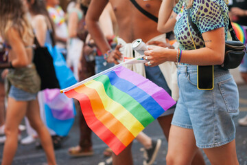 Rainbow pride flag closeup. Real people walking at Pride parade with rainbow flag as symbol of Pride month. Queer community march in the street with crowds