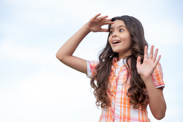 Surprised teen girl looking into distance keeping hand above eyes sky background, copy space
