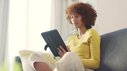 One young female freelancer smiling while browsing blogs, scrolling social media and streaming series online to enjoy on the weekend. Happy woman using a digital tablet on a sofa at home. - Powered by Adobe