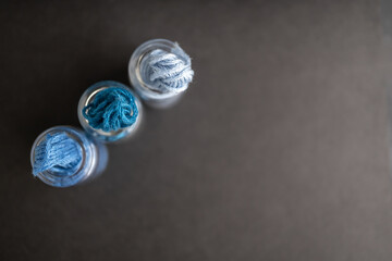 Obraz na płótnie Canvas detalle cenital de 3 frascos de vidrio llenos con madejas de hilo para bordar en colores azules, sobre gris obscuro, desbordándose