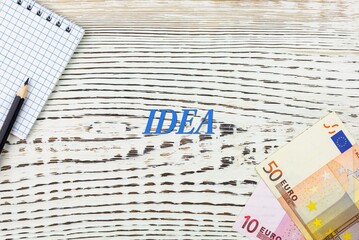 Naklejka premium IDEA - word (text) and euro money on a white wooden table, notebook, notepad. Business concept: buying, selling, commerce (copy space).