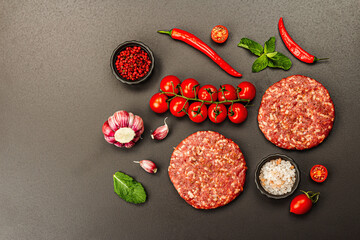 Raw steak cutlets from minced beef meat on black stone background. Fresh vegetables, mint