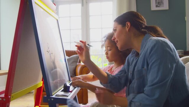 Mother and daughter having fun drawing picture on whiteboard at home together - shot in slow motion