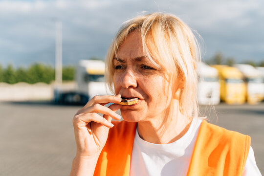 Middle Aged Portrait Of Worker Engineer Woman With Orange Vest Eating Cookies. Female Truck Driver 