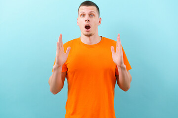 Young surprised man with an open mouth showing with both hands a big size sign, on a blue...