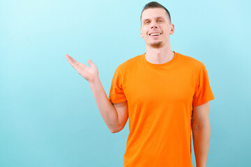 A smiling caucasian man in an orange t-shirt pointed a hand on the upper side. Showing empty copy...
