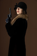 A 1920s woman wearing a black velvet coat with a fur collar and holding a gun