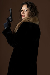 A 1920s woman wearing a black velvet coat with a fur collar and holding a gun