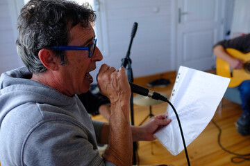 
middle-aged singer. Singer during a band rehearsal in the living room of a wooden house.
