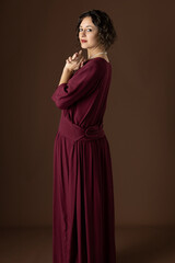 Fototapeta premium A 1920s woman wearing a dark red day dress against a plain studio backdrop