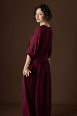 A 1920s woman wearing a dark red day dress against a plain studio backdrop