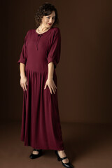 A 1920s woman wearing a dark red day dress against a plain studio backdrop